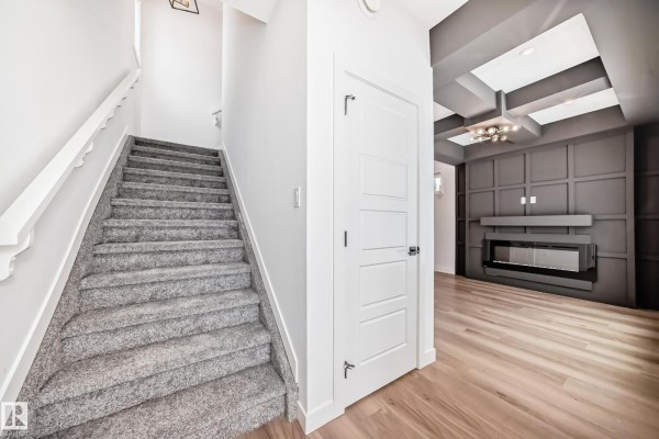 Interior view of a staircase with grey carpet and a door leading to a living room with a fireplace. - 11519 & 11521 67 St Nw, Edmonton