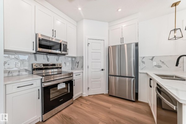 Modern kitchen with white cabinets, stainless steel appliances, a grey tile backsplash, and light wood flooring. - 11519 & 11521 67 St Nw, Edmonton