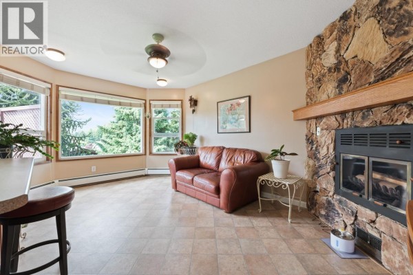 Cozy living room with a leather sofa, stone fireplace, and large windows. - 11523 Bonson Road, Pitt Meadows