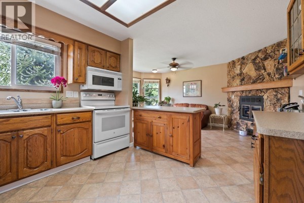 Kitchen with wooden cabinets, white appliances, and a view into the living room. - 11523 Bonson Road, Pitt Meadows