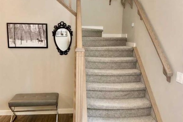 Interior staircase with gray carpet, light wood banister, and framed artwork on wall. - 1155 Kings Heights Way Se, Airdrie