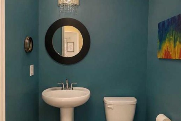 Powder room with teal walls, pedestal sink, round mirror, and a toilet. - 1155 Kings Heights Way Se, Airdrie
