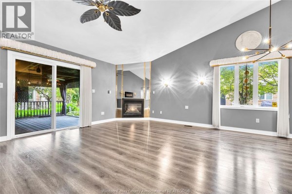 Spacious living room with a fireplace, sliding glass doors to a covered patio, and large windows. - 11568 Aldridge, Windsor