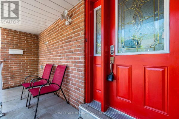 Close-up of a red front door with glass panels and two red chairs on the porch. - 1157 Kos Boulevard, Mississauga