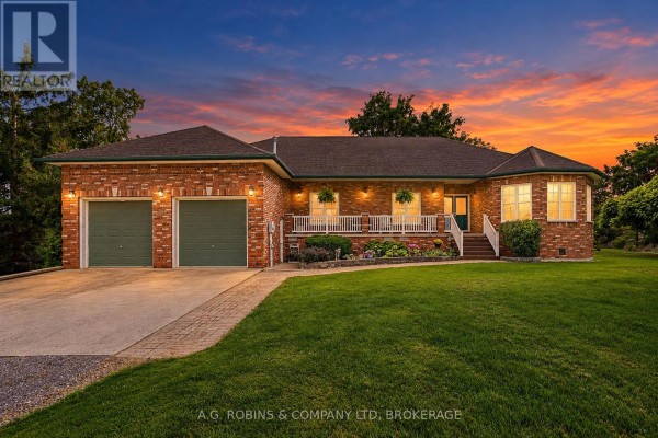 Front view of a brick bungalow with a porch, white railings, and a two-car garage at dusk. - 11573 3 Highway, Wainfleet