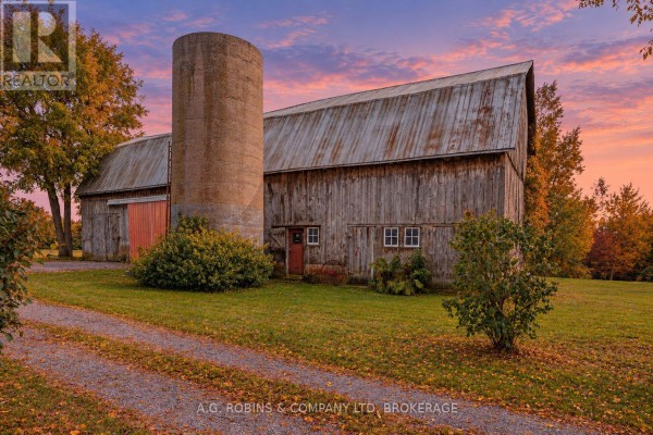A rustic wooden barn with a concrete silo and red barn doors stands on a grassy lawn. - 11573 3 Highway, Wainfleet