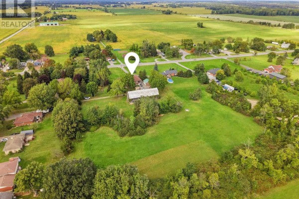 Aerial view of a property featuring a large house, barn, and expansive green lawns under a cloudy sky. - 11573 3 Highway, Wainfleet