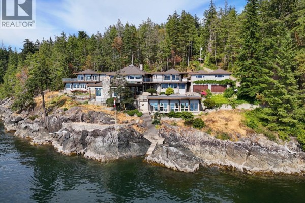 Front view of a sprawling house with multiple wings, large windows, and a stone chimney. - 11579 Sunshine Coast Highway, Halfmoon Bay