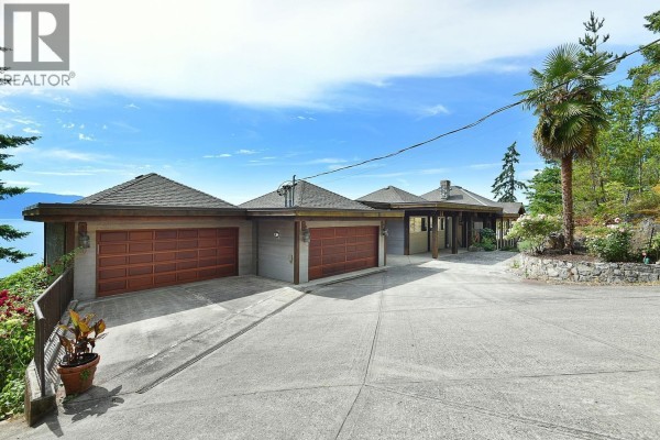Exterior view of a long, low house with a three-car garage and a paved driveway. - 11579 Sunshine Coast Highway, Halfmoon Bay