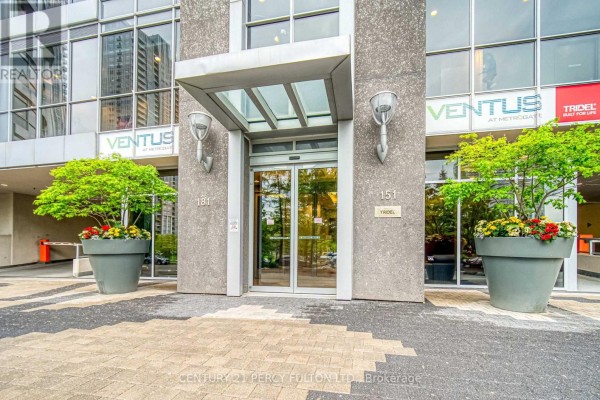 Entrance to the apartment building with glass doors, concrete pillars, and potted plants. - 116 - 181 Village Green Square, Toronto