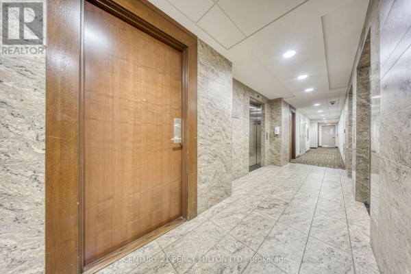 Interior building hallway with tiled floors, wood doors, and elevators visible in the distance. - 116 - 181 Village Green Square, Toronto