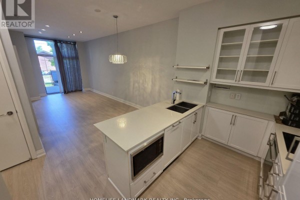 Open concept living area and kitchen with light wood floors, white cabinets, and island. - 116 - 21 Clairtrell Road, Toronto
