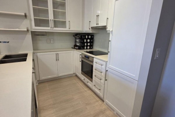 Modern white kitchen with stainless steel appliances, quartz countertops, and glass-fronted cabinets. - 116 - 21 Clairtrell Road, Toronto