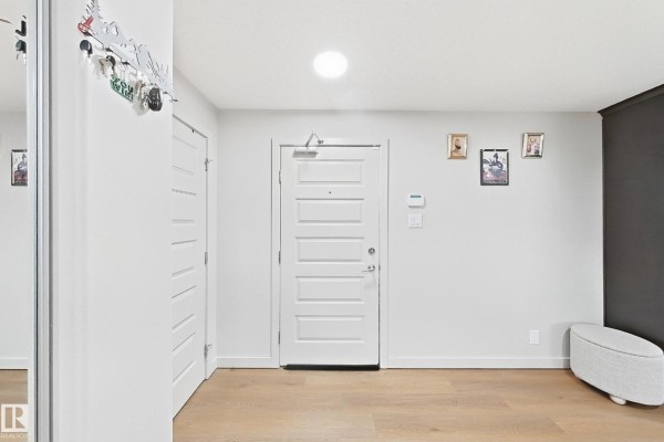 Foyer with white doors, light wood floors, and decorative items on the wall. - #116 4008 Savaryn Dr Sw Sw, Edmonton