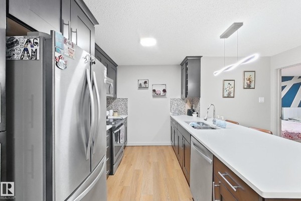 Modern kitchen with dark cabinets, stainless steel appliances, and a white island. - #116 4008 Savaryn Dr Sw Sw, Edmonton