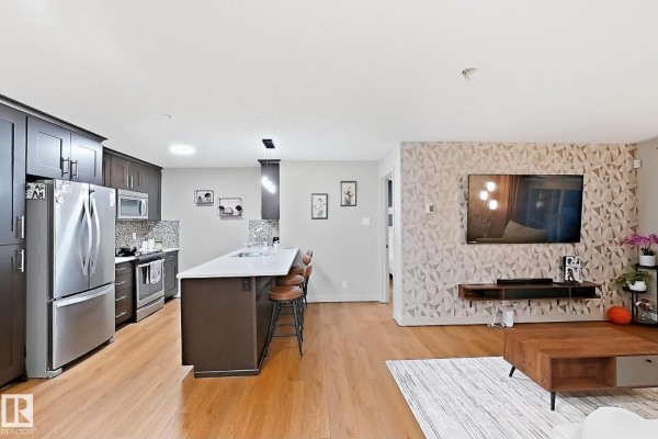 Open concept kitchen and living area with wood floors, island, and television. - #116 4008 Savaryn Dr Sw Sw, Edmonton