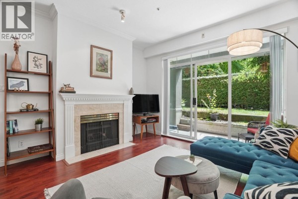 Living room with a fireplace, dark wood floors, and a sliding glass door leading outside. - 116 5835 Hampton Place, Vancouver