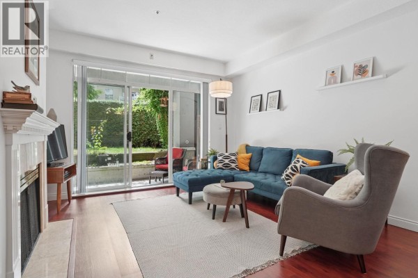Living room with a fireplace, blue sectional sofa, grey armchair, and sliding glass door. - 116 5835 Hampton Place, Vancouver