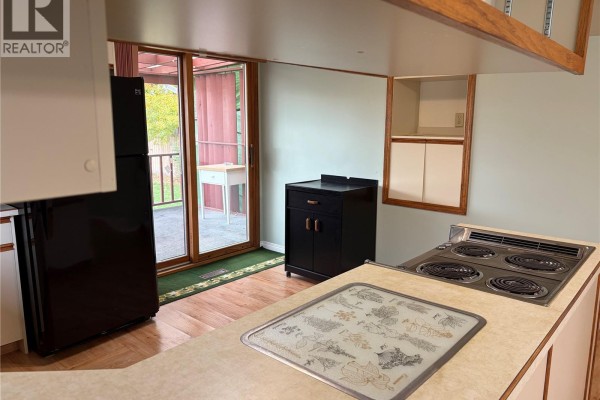 Kitchen with light wood cabinets, a black refrigerator, electric stove, and sliding glass door access to the backyard. - 116 5th Avenue E, Gravelbourg