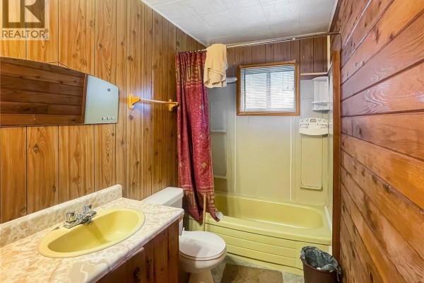 Bathroom with a yellow bathtub and toilet, light-colored vanity, and wood-paneled walls. - 116 Corrigal Drive, Turtle Lake
