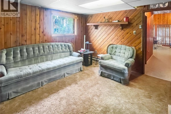 Living room with plush carpeting, a light blue sofa and armchair, and wood-paneled walls. - 116 Corrigal Drive, Turtle Lake