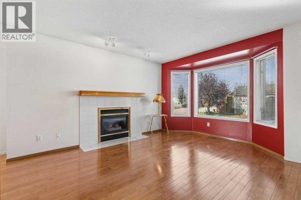 Living room with a gas fireplace, white tiled hearth, and a large bay window with red accent walls. - 116 Covington Rise Ne, Calgary