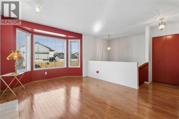 Living room with a white railing, red accent walls around the bay window, and a closet with red doors. - 116 Covington Rise Ne, Calgary