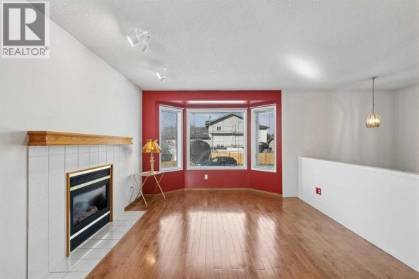 Living room with a gas fireplace, white tiled hearth, and a large bay window with red accent walls. - 116 Covington Rise Ne, Calgary