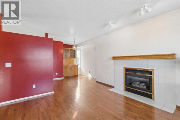 Living room with a gas fireplace, red accent wall, and a built-in wooden cabinet with glass doors. - 116 Covington Rise Ne, Calgary