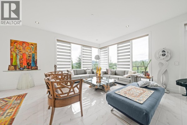 Spacious living room with a sectional sofa, large windows, patterned rug, and modern art. - 116 Deerview Lane, Anmore