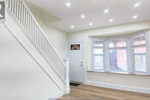 Interior entryway with white staircase, bay window, and light wood laminate flooring. - 116 Elm Avenue, Windsor