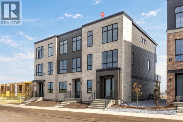 Side exterior of a new townhouse showing beige brick and gray siding. - 116 Greenwich Drive Nw, Calgary