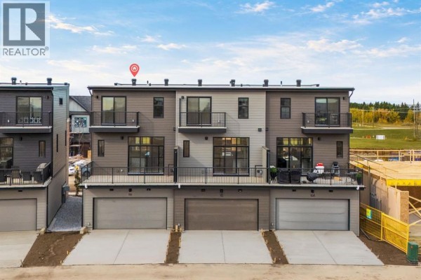 Rear exterior of townhouses with balconies, garages, and siding. - 116 Greenwich Drive Nw, Calgary