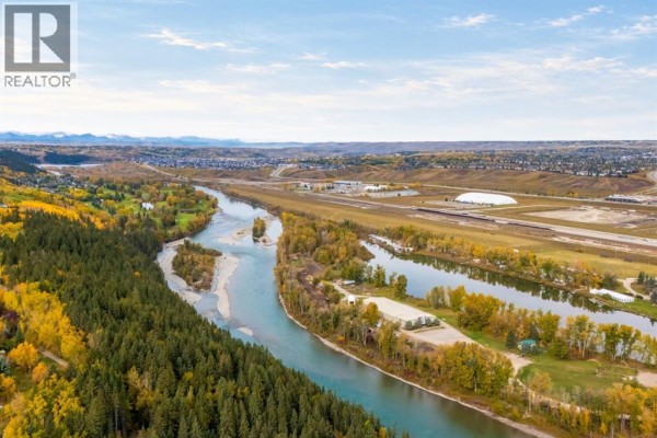 Aerial view of a river valley with trees, a city, and mountains. - 116 Greenwich Drive Nw, Calgary