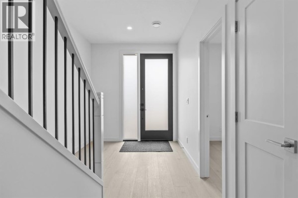 Interior entryway with white walls, light wood floors, and a black door. - 116 Greenwich Drive Nw, Calgary