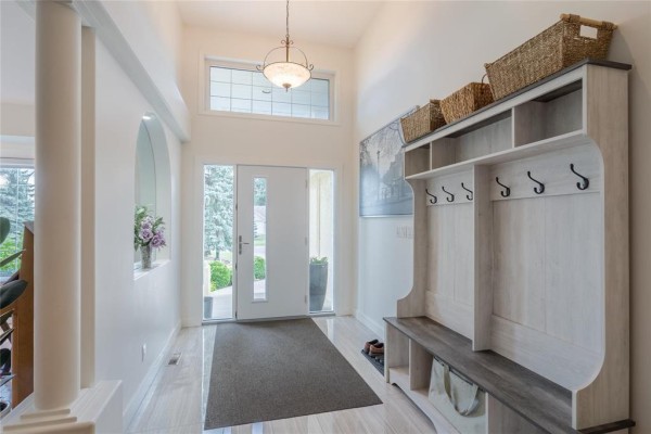 Bright entryway with a white bench and coat rack, a dark grey rug, and white tiled floors. - 116 Harvest Drive, Steinbach