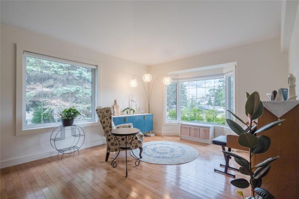 Living room with hardwood floors, two large windows, a bay window, and a blue cabinet. - 116 Harvest Drive, Steinbach