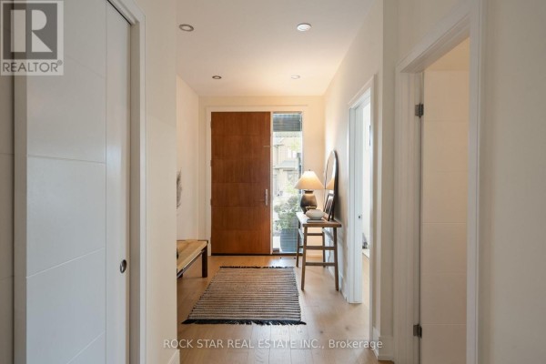 View down a bright interior hallway towards the front entrance with a wooden door and natural light. - 116 Lametti Drive, Pelham