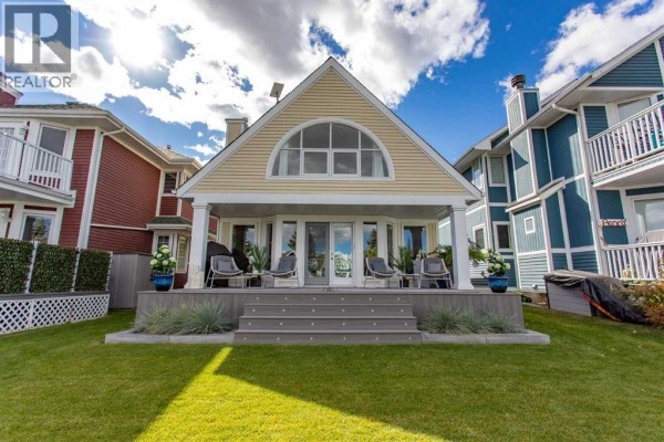Rear view of a yellow house with a covered porch and large arched window. - 116 Marina Bay Court, Sylvan Lake