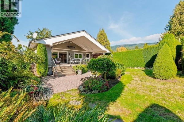 Exterior of a grey house with a covered porch and surrounding green landscaping. - 1160 14th Street, West Vancouver