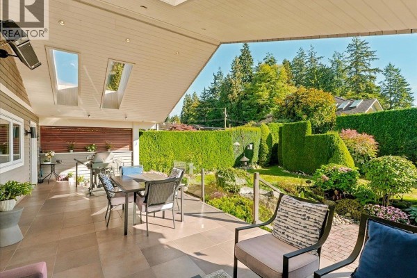 Tiled outdoor patio overlooking a garden with manicured hedges and trees. - 1160 14th Street, West Vancouver