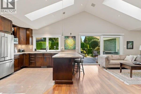 Kitchen and living area with vaulted ceiling, skylights, dark wood cabinets, and stainless steel appliances. - 1160 14th Street, West Vancouver