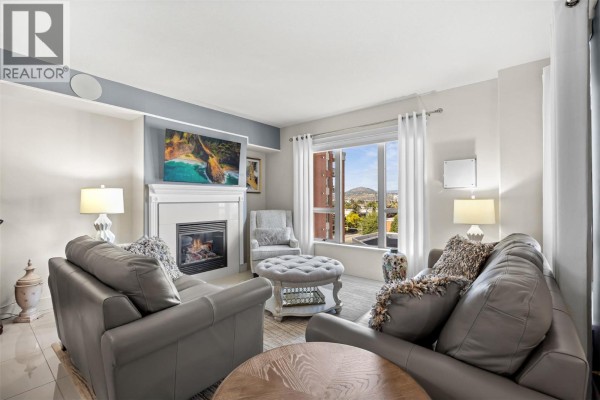 Living room showing gray leather couches, fireplace, armchair, ottoman, and window view. - 1160 Bernard Avenue Unit# 601, Kelowna