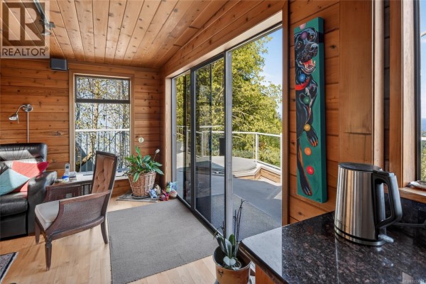Exterior view of a blue house with large windows and decks, surrounded by lush greenery. - 1160 Cappon Lane, Gabriola Island