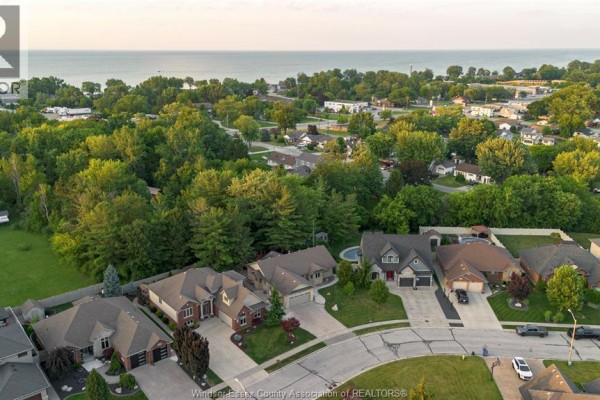 View of a paved driveway leading to a brick and stone ranch house with a garage and trees. - 1160 Jillian, Lakeshore