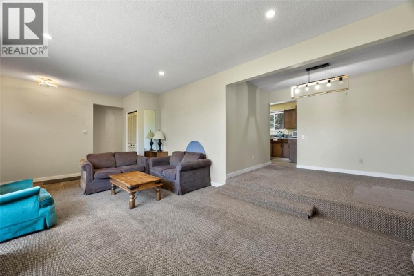 Living room with seating area, television, and a large window overlooking the backyard. - 1160 Kemano Street, Kamloops