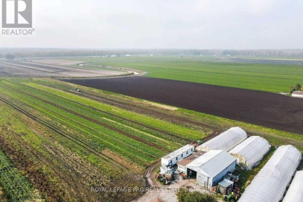 Wide aerial view of farm buildings, greenhouses, and cultivated fields under a hazy sky. - 1160 River Rd Road, Bradford West Gwillimbury