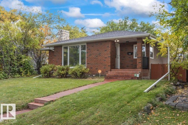 Side view of a red brick bungalow with a stone chimney and a sloped lawn. - 11631 130 St Nw, Edmonton