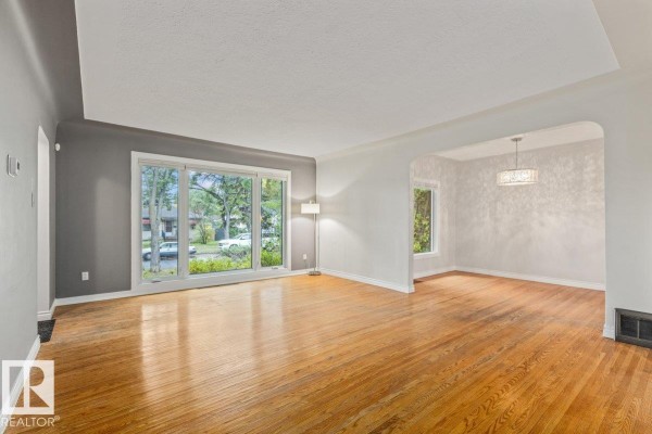 Living room with hardwood floors, large windows, and an adjacent dining area. - 11631 130 St Nw, Edmonton