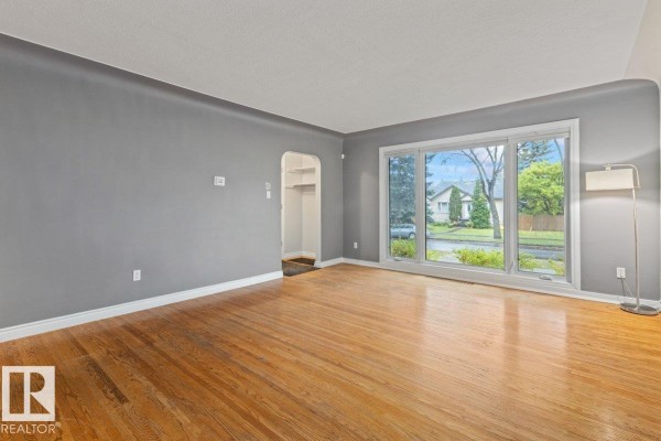 Living room with hardwood floors, large windows offering a street view, and gray walls. - 11631 130 St Nw, Edmonton